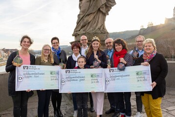 Von links: Christin Schnfu (Albert-Schweitzer Kinderdrfer), Gwendolyn, Petra Winkler (Albert-Schweitzer-Kinderdrfer), Kerstin Wolf, Max, Cornelius Lauter (geschftsfhrender Vorstand der GWF), Carolin Meyer (frnkische Weinknigin), Alfred Hackenberg (Warenbereichsleiter EDEKA Nordbayern-Sachsen-Thringen ), Ina Schmolke (1. Vorsitzende KIWI e.V.) , Stefan Wolf (KIWI ev.), Monika Wohlfart (KIWI ev.) bei der Spendenbergabe auf der alten Mainbrcke in Wrzburg.