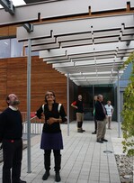 Wie ein verlängertes Vordach leitet die Plastik von Sabine Straub (zweite von links) in das neue Analytikgebäude der Bayerischen Landesanstalt für Weinbau und Gartenbau in Veitshöchheim. Die paarweise angeordneten und sich zugewandten Aluminiumlamellen offenbaren ihr Geheimnis erst bei genauerem Hinsehen: In ihrem Innern sind sie farblich gestaltet: Ein Weg, der vom Zartgrün im Foyer hinaus über Sommer und Herbst bis in den Winter führt. Die Formen der Lamellen mit ihren Einschnitten sollen nicht nur an die traditionell kleinparzellige fränkische Landschaft erinnern,erklärte Straub bei der Präsentation ihres Werkesdem Leiter des Fachzentrums Analytik, Josef Valentin Hermann (links im Bild). Sie können auch Assoziationen an schmale Farbstreifen und -sequenzen bei Chromatographieanalysen wecken oder an Dünnschnittpräparate von organischen Strukturen erinnern. Leider fehlte bei der Vorstellung dieses Werkes eine von Sabine Straub fest eingeplante Mitgestalterin: die Sonne. Ihre Strahlen werden für ein lebhaftes Schattenspiel sorgen und auch die Farben aufleuchten lassen.