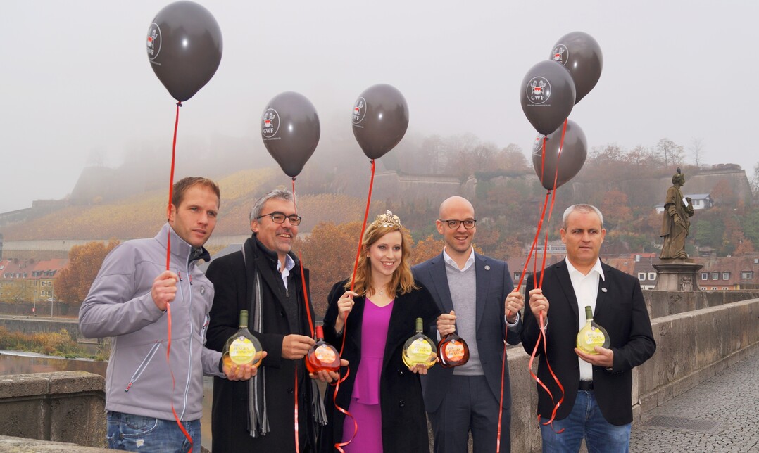 Kellermeister Sebastian Knott, Vorstandsvorsitzender Andreas Oehm, fränkische Weinkönigin Klara Zehnder, geschäftsführender Vorstand Cornelius Lauter und stellvertretender Vorstandsvorsitzender Martin Geißler präsentieren den neuen Jahrgang der "Jungen Fank"n" auf der alten Mainbrücke.